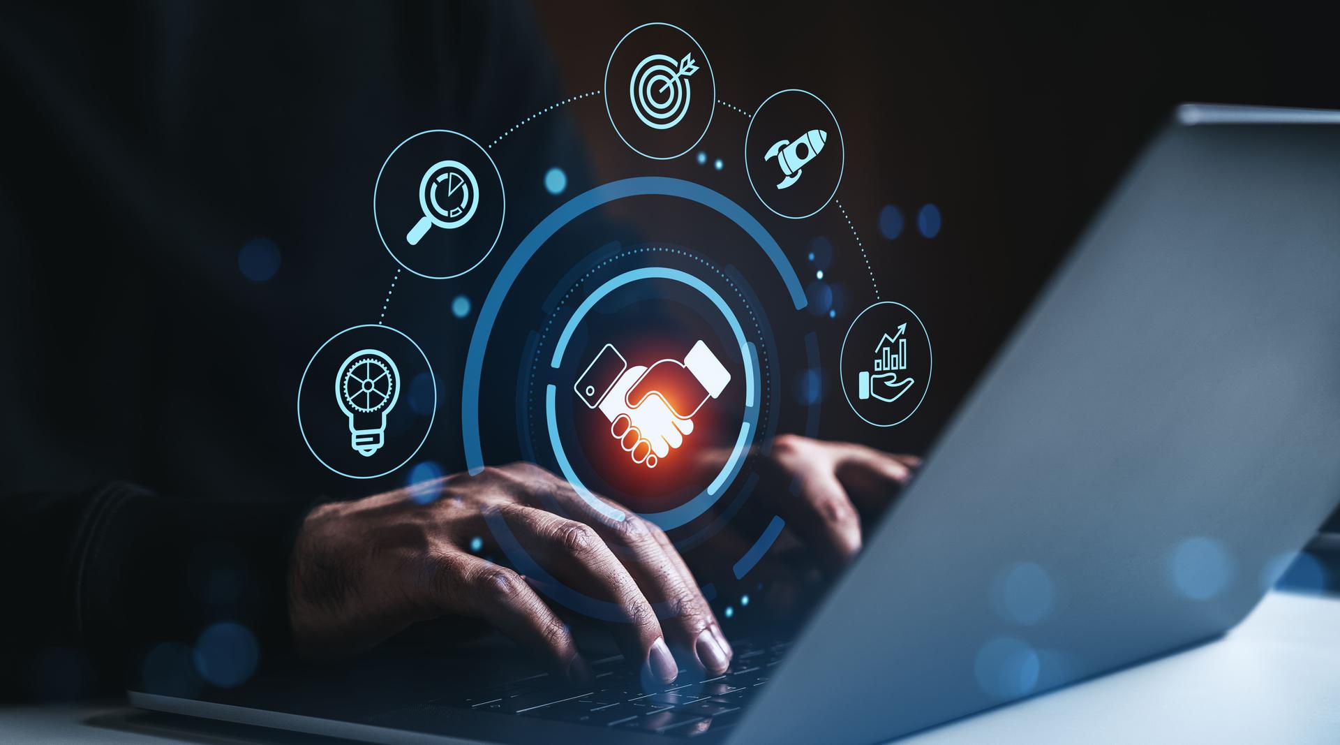 Business partnership and digital marketing concept with handshake and strategy icons over laptop keyboard in futuristic glowing interface style..
